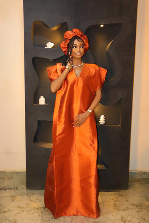 Woman in orange satin African Mikado boubou dress with matching headband, standing indoors