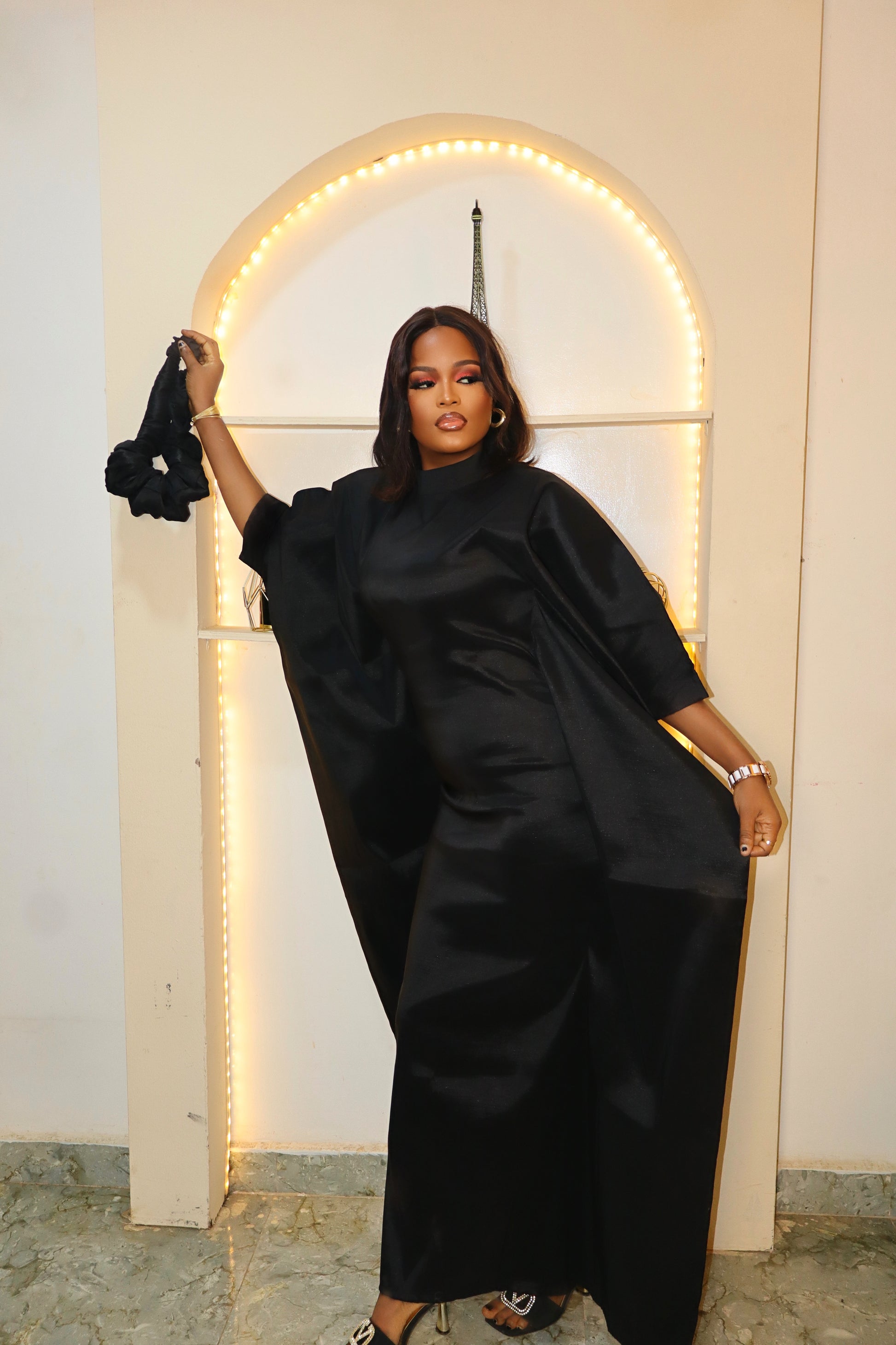 Woman in a black Boubou dress standing in front of a lit archway.