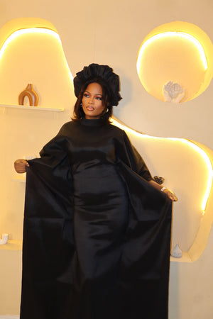 Woman in a black Boubou dress standing in a room with decorative lighting.