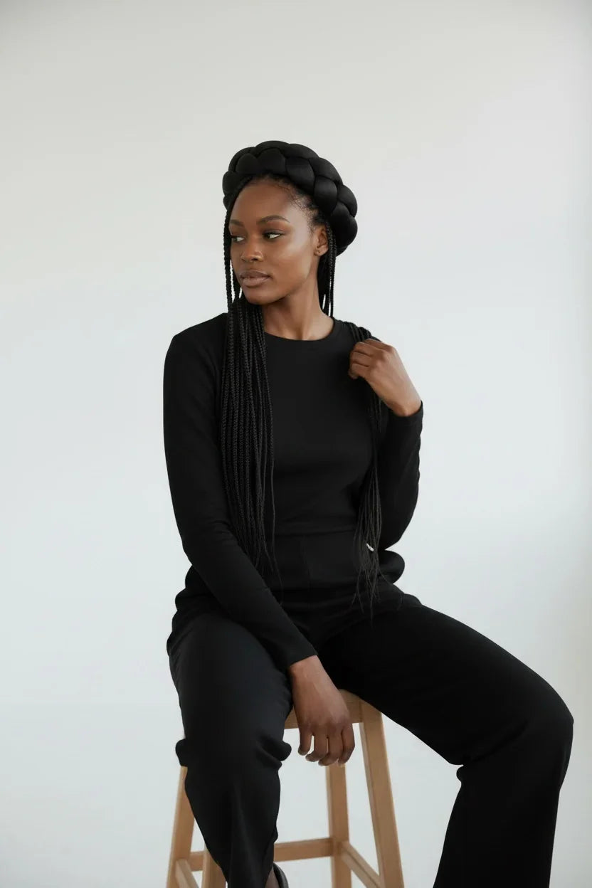 Woman in a black outfit sitting on a stool against a white background