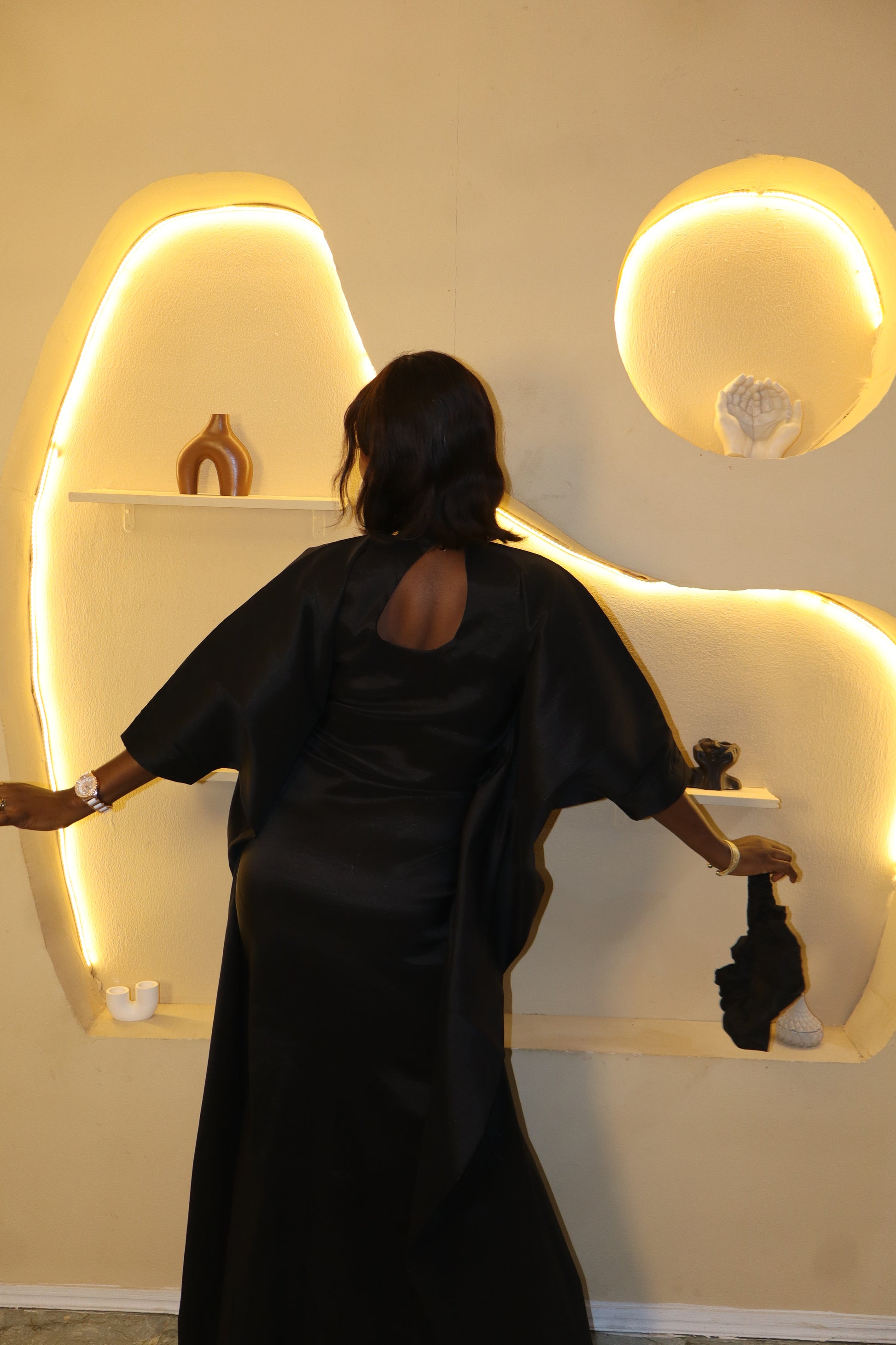 Woman wearing a black dress standing in front of a decorative wall with illuminated arches.